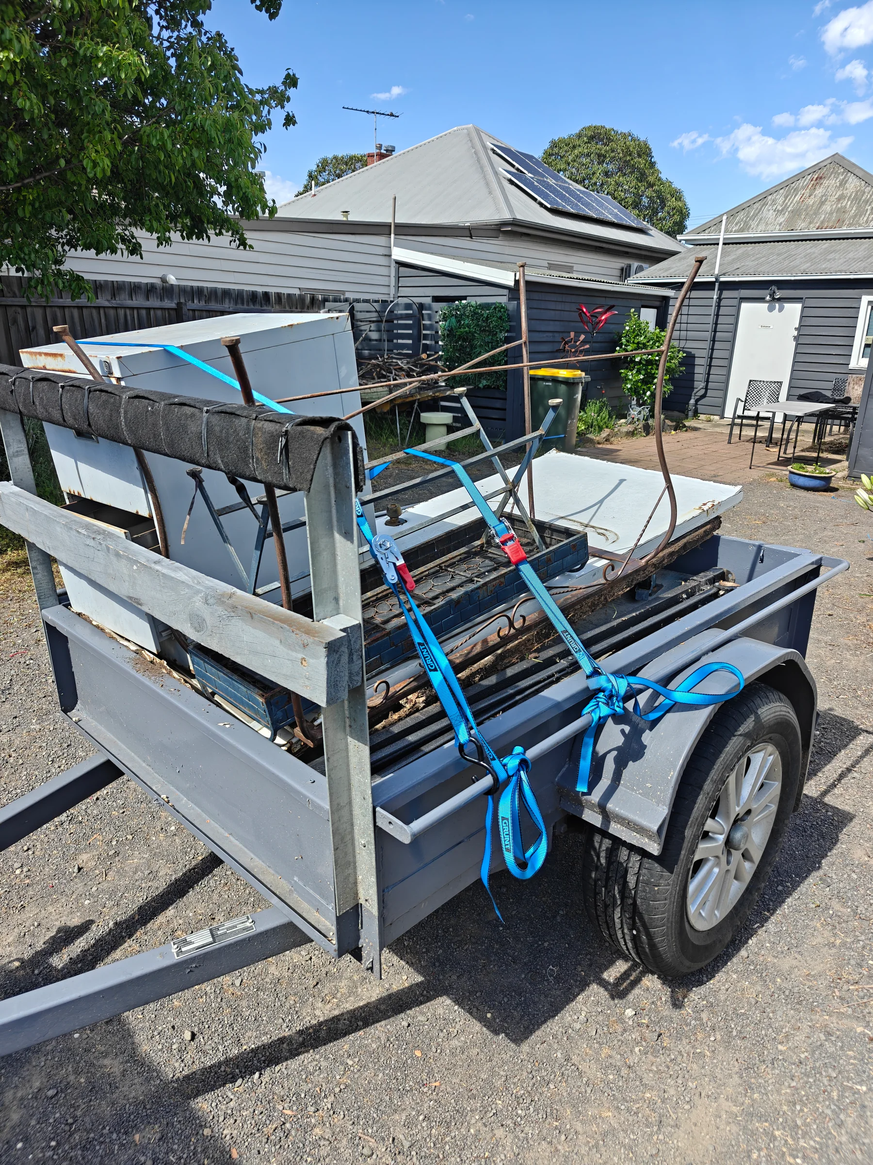 A trailer loaded with metal household items and secured with blue straps.